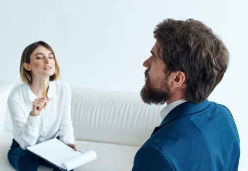 A man in a blue jacket and a beard talks to a woman on the sofa indoors. High quality photo