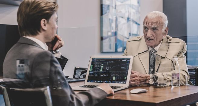 Young financial advisor sitting in front of laptop, consulting senior client with his investment strategy.