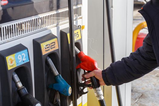 Tula, Russia - February 6, 2021: Old man hand taking red 95 gasoline fuel nozzle from gas station at day light.