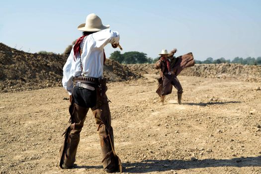 Two cowboy outfit costume with a gun held in the hand on gun fight against smoke and sun light on the buttle field.