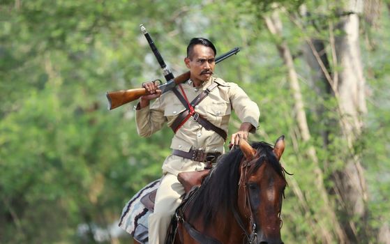 The men wearing Asian police outfit costume with a gun held in the hand riding horse in forest background.