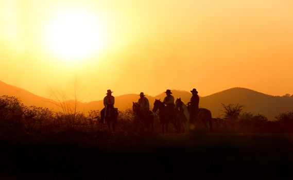 The silhouette of  rider as cowboy outfit costume with a horses and a gun held in the hand against smoke and sunset background