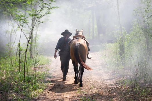 The silhouette of  rider as cowboy outfit costume with a horses and a gun held in the hand against smoke and sunset background