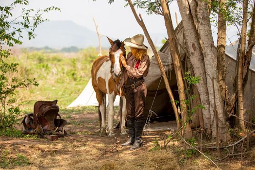 Cowgirl standing by horse at outdoor farm. 