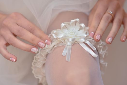 Slender sexy bride puts a garter on her leg close-up. The bride's fees for the wedding. Preparation for the wedding celebration.
