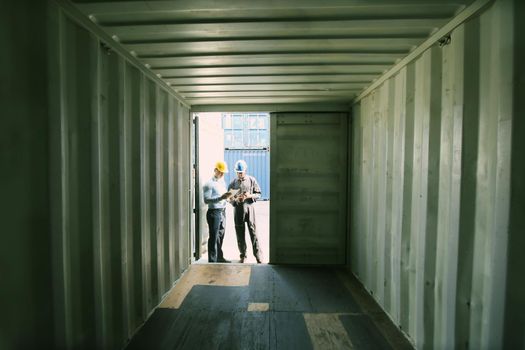 Manager and dock worker under discussion about dock container shipping warehouse document, they wearing safety uniform hard hat ,face mask and hold radio communication.