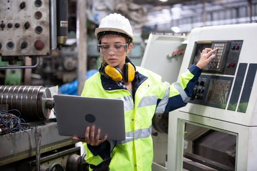 Woman worker wearing safety goggles control lathe machine to drill components. Metal lathe industrial manufacturing factory