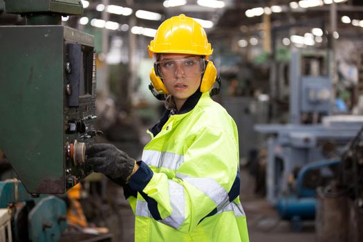 Woman worker wearing safety goggles control lathe machine to drill components. Metal lathe industrial manufacturing factory