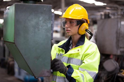 Woman worker wearing safety goggles control lathe machine to drill components. Metal lathe industrial manufacturing factory