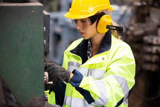 Woman worker wearing safety goggles control lathe machine to drill components. Metal lathe industrial manufacturing factory