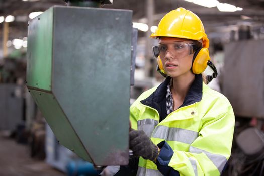 Woman worker wearing safety goggles control lathe machine to drill components. Metal lathe industrial manufacturing factory