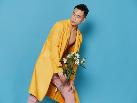 Attractive Asian man in a yellow coat and pink trousers with a bouquet of flowers in his hand. High quality photo