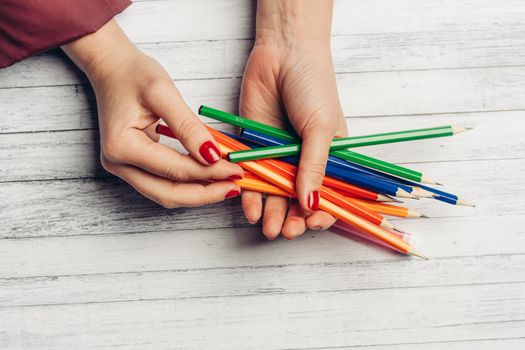 bright colored pencils in female hands wooden background texture gray color. High quality photo