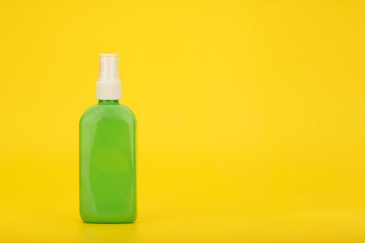 Minimalistic still life with sunscreen spray against yellow background with copy space. Sunscreen product for tanning in green plastic tube. High quality photo