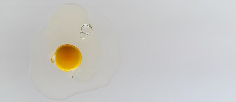 Cracked chicken egg with yolk and albumen on transparent surface and white background.