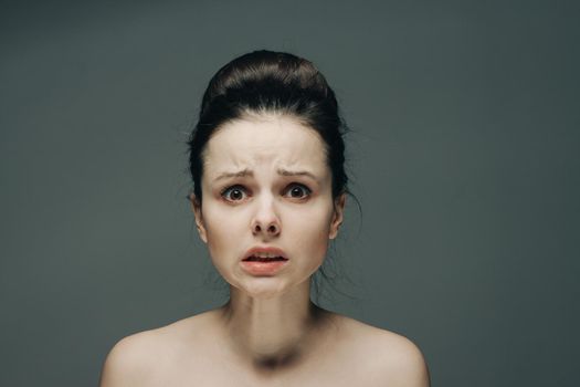 frightened woman's face naked shoulders hairstyle gray background model. High quality photo