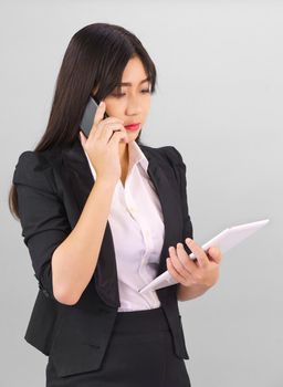 Young Asian women in suit standing using her digital tablet and phone against gray background