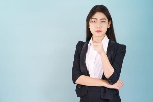 Asian woman looking at camera and pointing finger on blue background