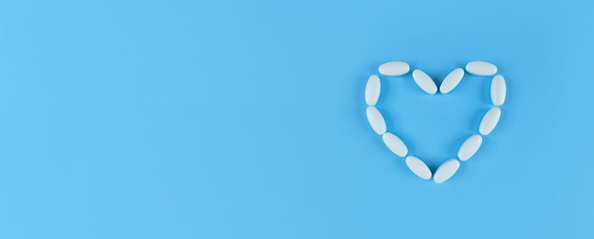 Heart shape made from white tablets on a blue backdrop with copy space.
