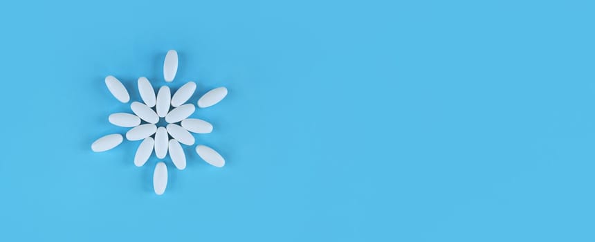 Flower shape made from white tablets on a blue backdrop with copy space.