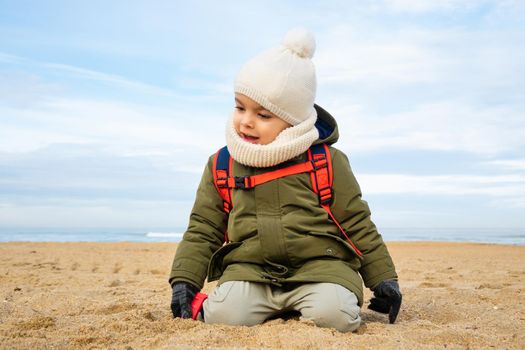 Little boy playing in the sand on beach in winter