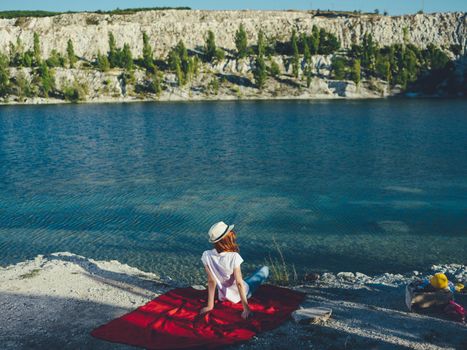 A woman sits on a red cloth near the river and a hat on her head. High quality photo