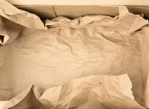 open empty rectangular brown cardboard box for transportation and packaging of goods, top view. At the bottom is a piece of brown paper
