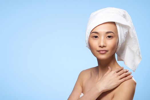 pretty woman asian appearance bare shoulders towel on head spa procedure blue background. High quality photo