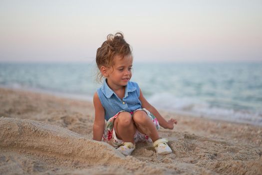 Child playing sand beach Little girl play sad alone summer family vacation Caucasian female 3 years old dressed denim near sea water