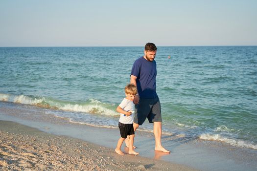 Dad holds son hand. Father Child spending time together sea vacation Young man little boy walking beach Fathers day. Family with one child. Happy childhood with daddy. Full lenght