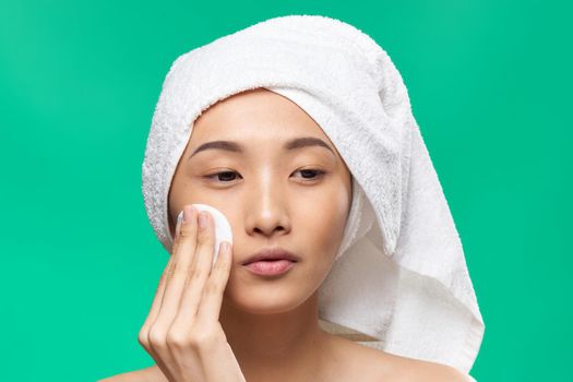 woman with a towel on her head wipes her face with a cotton pad Green background. High quality photo