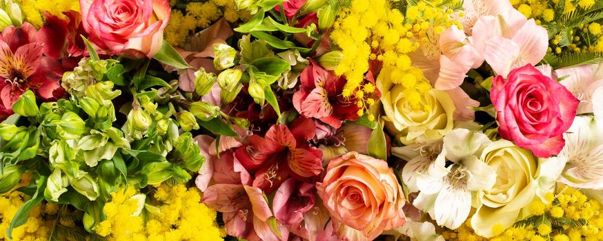 Close up fresh spring flowers. Mimosa, roses. Yellow red vivid background. Flat lay, top view