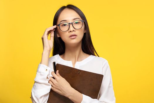 Business woman in glasses with notepad in hands executive secretary yellow background. High quality photo