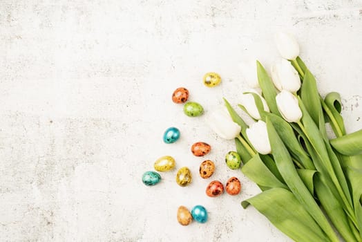 Easter and spring concept. Top view of white tulips and colored easter eggs on concrete backgrund with copy space