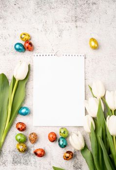 Easter and spring concept. Top view of white tulips, blank calendar and colored easter eggs on concrete backgrund with copy space
