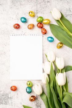 Easter and spring concept. Top view of white tulips, blank calendar and colored easter eggs on concrete backgrund with copy space