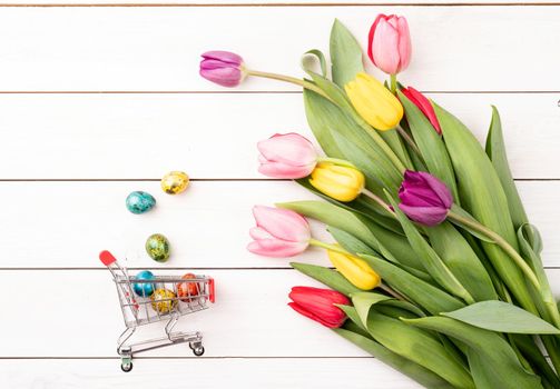 Holiday shopping. Shopping cart with colorful bouquet of tulips on white wooden background