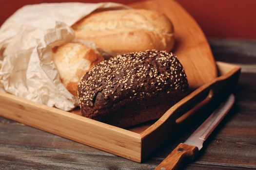 flour products rye bread on a tray and a sharp knife on a table on a red background. High quality photo