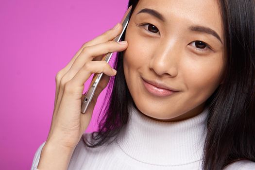 woman asian appearance talking on the phone close-up studio pink background smile. High quality photo