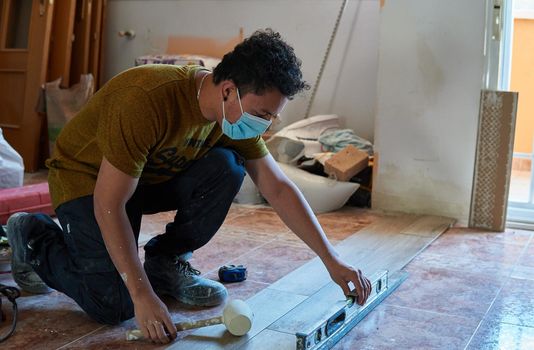 Mason tiling a room with a mustard-colored t-shirt and rubber pot and level and with a mask