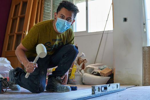 Mason tiling a room with a mustard-colored t-shirt and rubber pot and level and with a mask