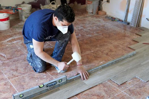 Bricklayer tiling a room with rubber pot and level and with mask