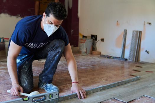 Bricklayer tiling a room with rubber pot and level and with mask