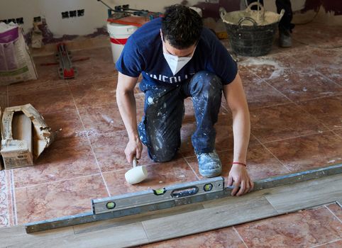 Bricklayer tiling a room with rubber pot and level and with mask