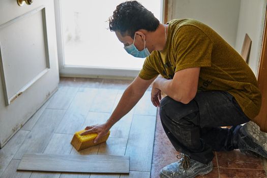 Worker cleaning the floor with a sponge and protective mask next to a door