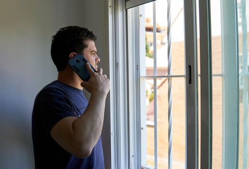 Man talking on a cell phone in a room next to a window