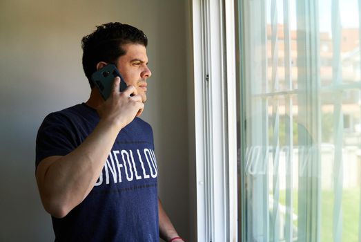 Man talking on a cell phone in a room next to a window