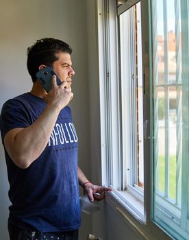 Man talking on a cell phone in a room next to a window