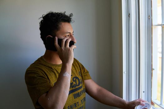 Man talking on a cell phone in a room next to a window