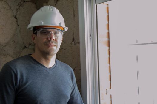 Bricklayer with helmet, protective goggles and grey sweatshirt in a reform